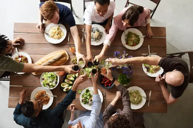 Eine Gruppe verschiedenen Alters stößt über einer langen gedeckten Tafel miteinander an