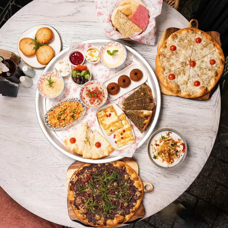 Von oben fotografierter runder Tisch mit Brot, Hummus, Falafel, Käse und mehreren Schalen zum Teilen